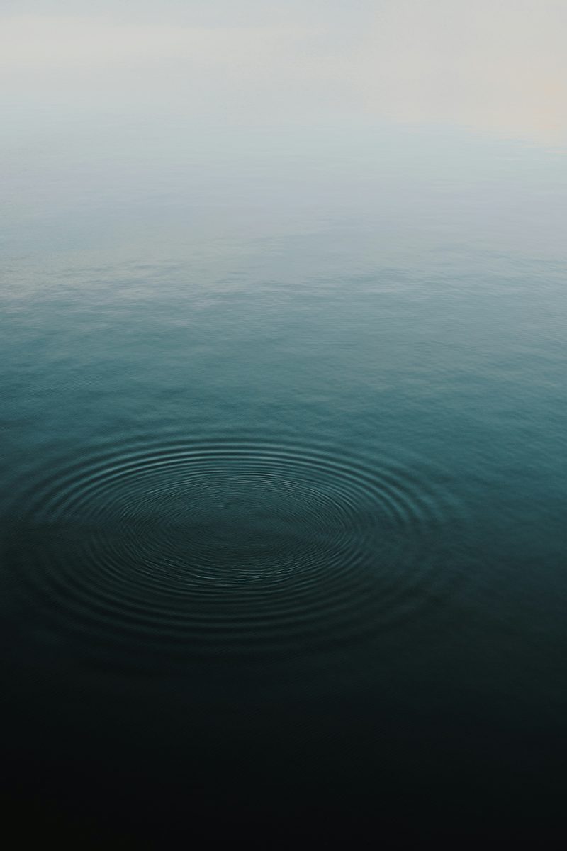 Still teal water with a single set of soft ripples spreading outward