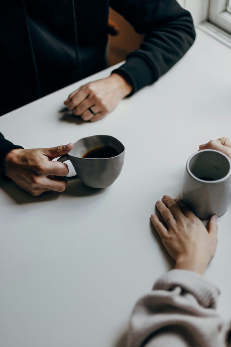Two people sitting across a table with coffee, hands resting near their cups