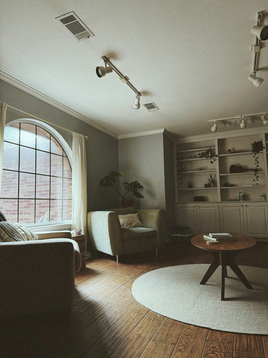 A quiet sitting room with armchairs, an arched window, plants and a round rug