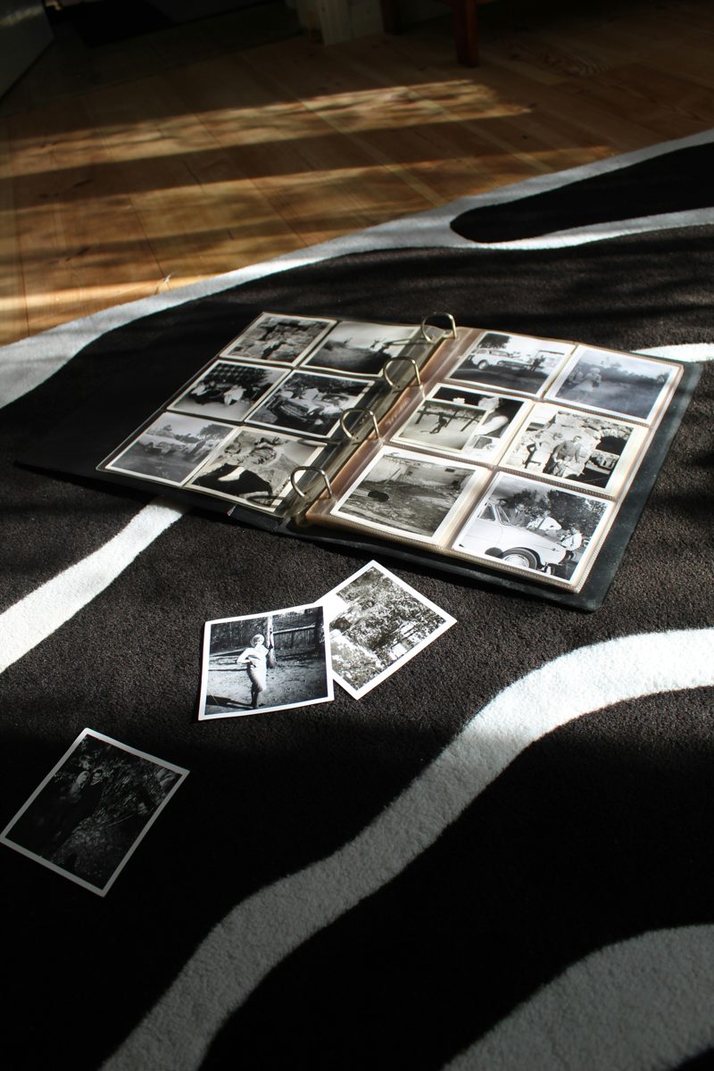 An open album of old black-and-white photographs on a rug, with loose prints nearby in afternoon light