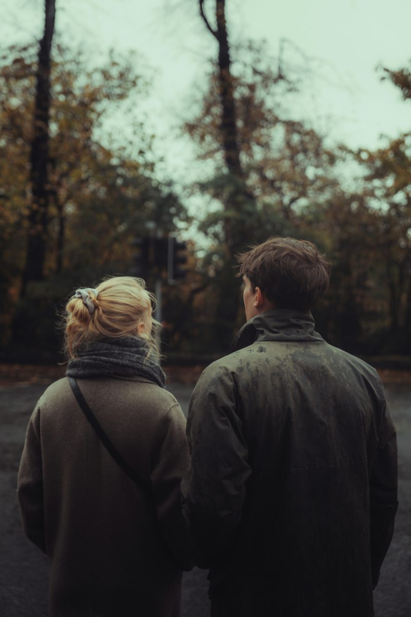 Two people standing side by side, seen from behind, looking toward autumn trees
