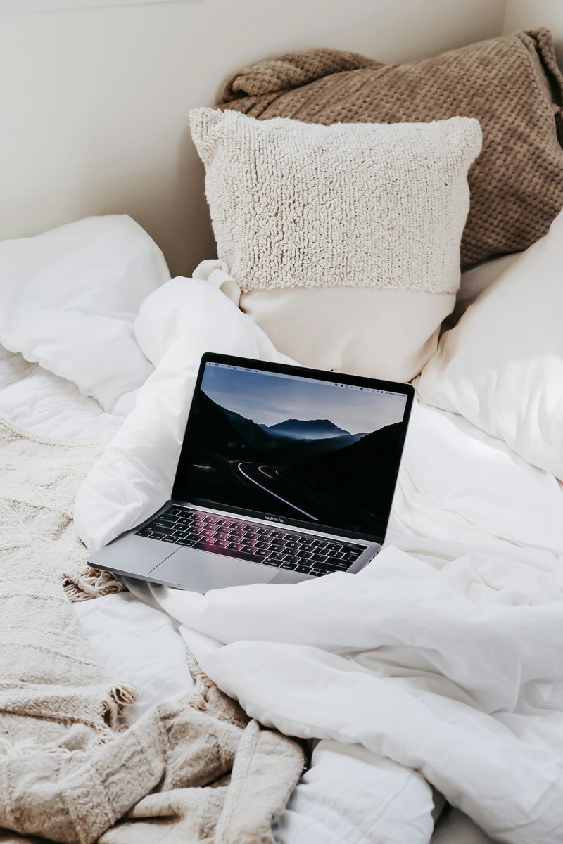 A laptop resting on a cozy bed with soft pillows and blankets, ready for an online therapy session